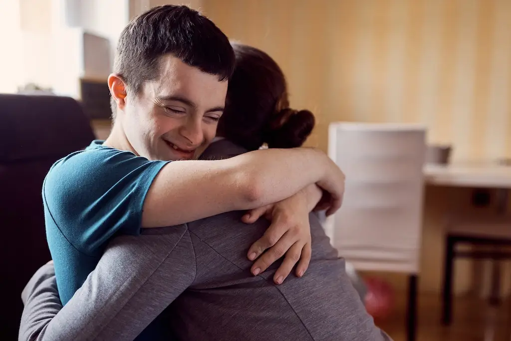 A young man with Down syndrome smiles while hugging a woman, illustrating the supportive nature of life skills development